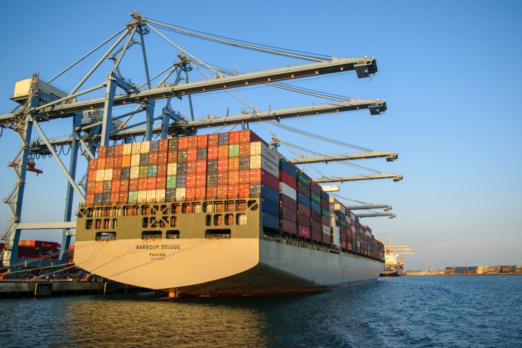 pexels photo 24246926 24246926 A large container ship at an industrial harbor with cranes under a clear blue sky.
